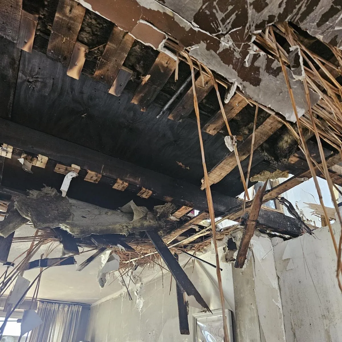 Ingestort plafond met verkoolde balken en losgebrande isolatie na een woningbrand