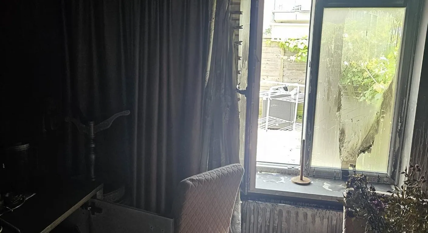 Donkere kamer na een brand met roet op gordijnen en meubels en een beslagen raam