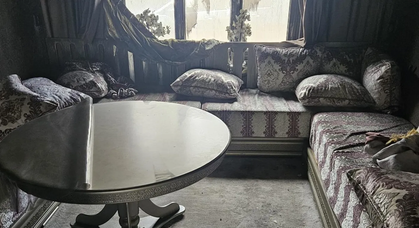Zithoek na een woningbrand: bank, tafel en vloerkleed grijs van het roet, met brokstukken op de vloer