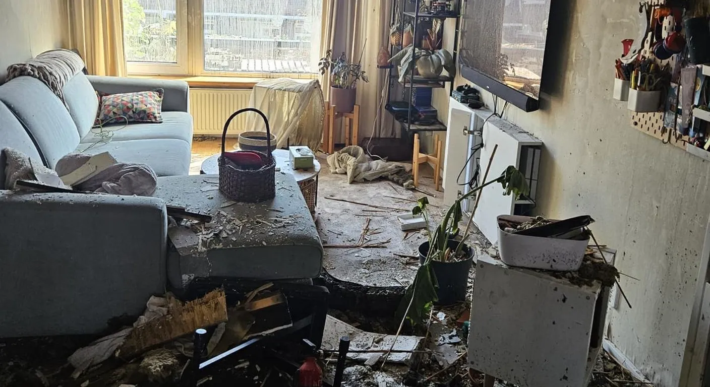 Woonkamer na een brand met puin van het plafond op de bank en de vloer en roet op de wanden